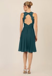 Teal jurk met bloemenkant details, een keyhole rugontwerp en een vloeiende rok. Gecombineerd met zilveren bandenhakken.