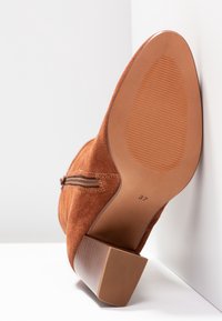Bottine en daim marron avec un talon carré, fermeture éclair sur le côté et semelle texturée. Taille marquée 37 au-dessous.
