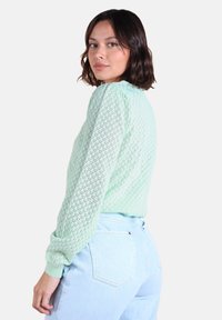 Pull en tricot vert menthe avec un motif en losanges texturé, à manches longues et avec des poignets côtelés, associé à un jean taille haute bleu clair.