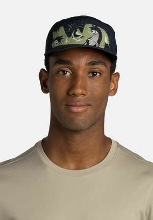 Young man wearing a black and green cap with animal designs and a beige crew-neck shirt, facing forward with a neutral expression.