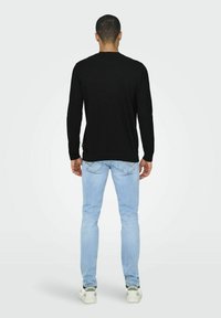 Czarna koszula z długim rękawem, dopasowany krój, w połączeniu z jasnoniebieskimi slim fit dżinsami, białe sneakersy z zielonymi akcentami, widok z tyłu.