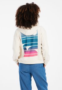 Felpa color crema con un vivace motivo di righe e cerchi blu e rosa sul retro. Tessuto morbido e accogliente, vestibilità rilassata.