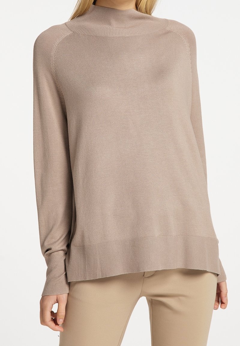 Beige lange mouw trui met een hoge geribbelde halslijn, iets oversized pasvorm en geribbelde manchetten, gemaakt van een gladde, lichte breiselstof.