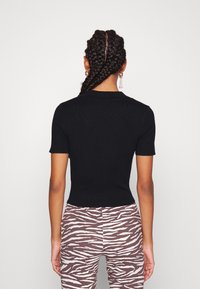 Polo preto de manga curta com um design ajustado, confeccionado em material canelado. Usado com leggings com estampado de zebra em marrão e branco.