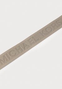 Beige tygrem med präglad "MICHAEL KORS" text, med en ribbad textur. Enkel, platt design som passar för accessoarer.