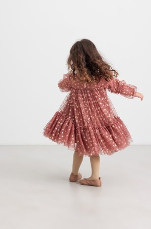 Lyserød tylkjole med gyldne blomstermotiver, puffede ærmer og flæsekant. Båret med beige strømpebukser og bløde lyserøde sko.