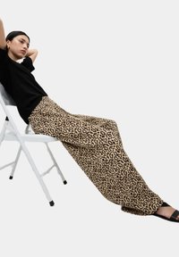 Kalhoty s širokými nohavicemi v leopardím vzoru s hladkým povrchem, s béžovým podkladem a tmavě hnědými skvrnami. Doplněné černým topem a sandály.