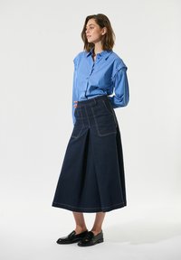 Blauwe gestreepte button-up blouse gecombineerd met een donkerdenim rok met een brede silhouette, voorzakken en contrasterende stiksels.
