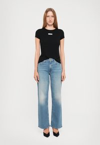Zwarte fitted t-shirt met korte mouwen en een klein logo. Lichtblauwe wijde spijkerbroek met een vervaagde wassing en een standaard vijf-pocketontwerp.