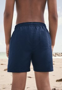 Tmavomodré plavkové šortky s elastickým pásom, bočnými vreckami a zadným nášivkovým vreckom vybaveným kovovým okom.