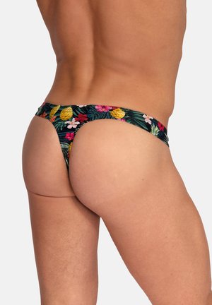 Homme portant un maillot de bain de style string avec imprimé tropical floral et ananas, vu de dos et de côté sur un fond uni.