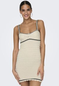 Beige crochet dress featuring thin straps, black accents along the neckline and hem, and a fitted design with ribbed texture.