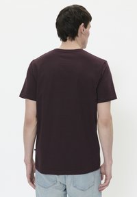 Camiseta corta de manga de color marrón con escote redondo y un acabado texturizado, combinada con jeans de mezclilla azul claro. Sin logotipos ni patrones visibles.