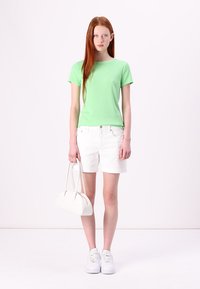 Lys grøn ribbet T-shirt, hvide denim shorts, hvide sneakers og en hvid håndtaske. Outfittet har et enkelt design og bløde teksturer.