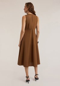 Brown sleeveless dress with a flared silhouette, back zipper, and smooth fabric. Paired with black strappy heels. Simple and elegant design.