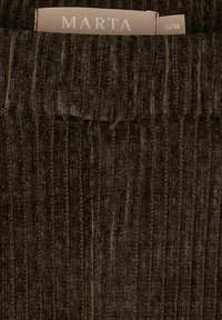 Mørkebrunt kordfløjlstof med lodrette riller. Mærket lyder "MARTA" og størrelse "S/M" fastgjort til den øverste kant.