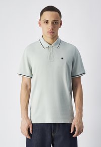 Jasnozielona koszulka polo z czarnym wykończeniem przy kołnierzyku i rękawach, z małym logo po lewej stronie klatki piersiowej. Wykonana z bawełny, krótki rękaw.