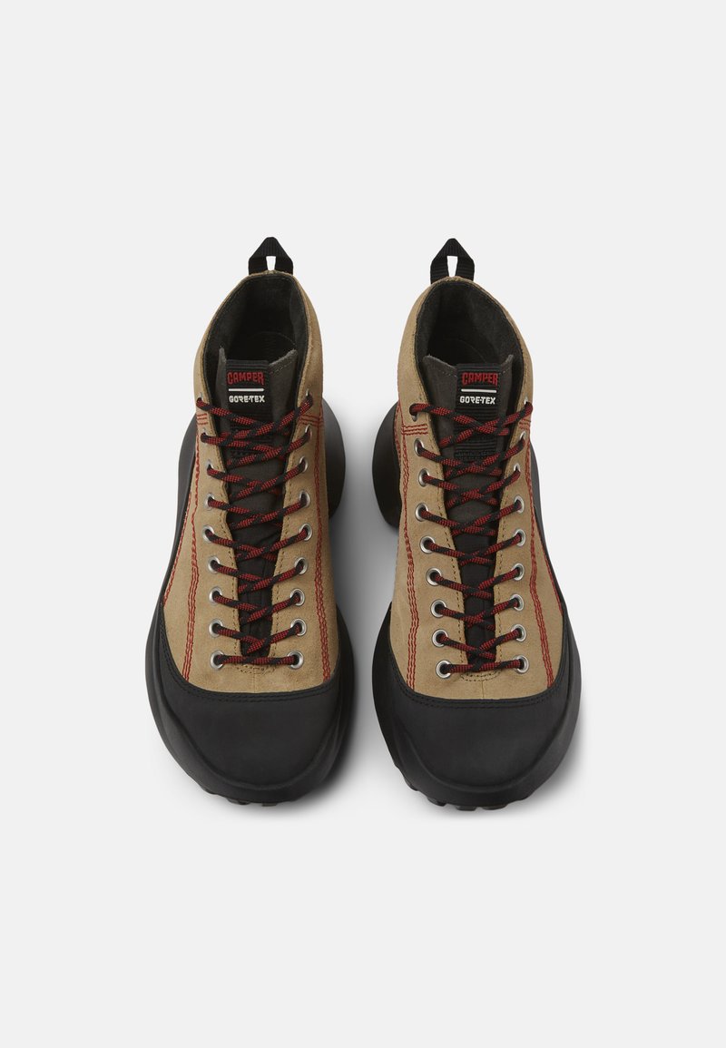 Scarpe da trekking alto in marrone con suole in gomma nera, lacci rossi e neri, cuciture rosse e targhe "Camper Gore-Tex" sulle linguette.