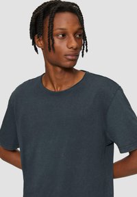 Donkergrijze katoenen T-shirt met korte mouwen, ronde hals en een licht vervaagde textuur. Heeft zichtbare stiksels langs de randen.