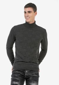 Dunkelgrauer Rollkragenpullover aus Strickstoff mit einem strukturierten Muster und gerippten Bündchen, kombiniert mit zerrissenen schwarzen Jeans.