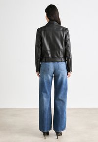 Must musta jakker, millel on keha lähedane lõige ja lukuga varrukad, kombineeritud kõrge vöökohtadega siniste denimite flared teksadega, millel on gradient pesu.