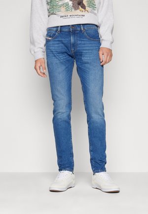 Mann trägt blaue, schmal geschnittene Jeans, weiße Turnschuhe und ein hellgraues Sweatshirt mit einem Adler und dem Schriftzug "Smoky Mountains".