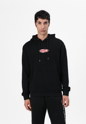 Svart hettegenser laget av bomull med en frontlomme, med en rød og hvit "Guess Jeans" logo på brystet.