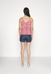 Débardeur floral rouge avec des bretelles fines et un dos en V, associé à un short en denim foncé. Tissu lisse avec une coupe décontractée.