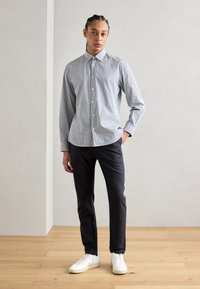 Striped button-up shirt in blue and white, paired with dark pants and white sneakers. Features a collar and long sleeves.