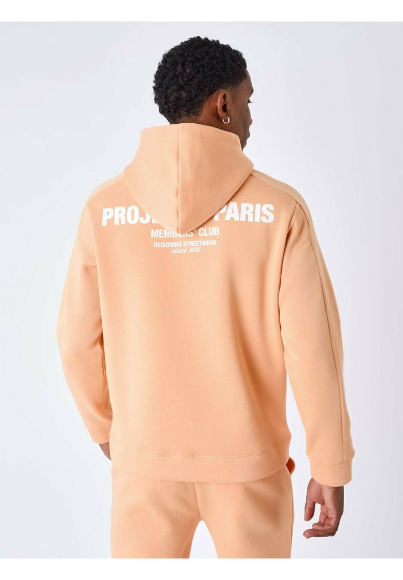 Sudadera con capucha de color melocotón en tejido suave, con el texto blanco "PROJECT PARIS MEMBERS' CLUB" en la parte posterior. Diseño ajustado, mangas largas.