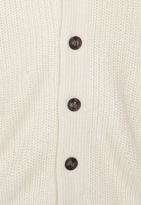 Krémový pletený kardigan s žebrovanou strukturou, pěti tmavě hnědými knoflíky vpředu a volným střihem.