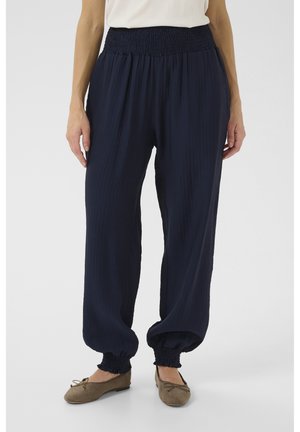 Pantaloni leggeri, plissettati, di colore blu navy con vita arricciata e polsini elasticizzati alle caviglie. Abbinati a ballerine neutre.