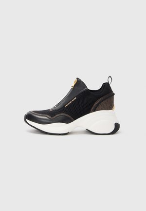 Sneaker nera in rete e pelle con suola bianca spessa, caratterizzata da un accentuato zip dorato e dettagli marroni. Supporto alla caviglia imbottito.