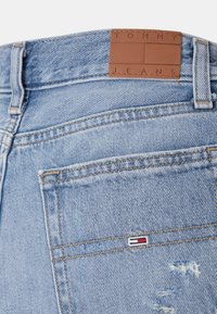 Jeans in denim azzurro chiaro con una texture consumata, dotati di un'etichetta in pelle marrone con la scritta "TOMMY JEANS" sulla vita.