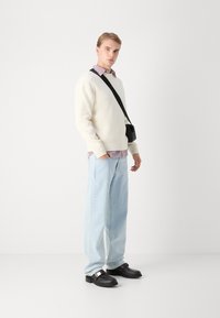 Suéter blanco acanalado sobre una camisa a cuadros roja y blanca, jeans azul claro y zuecos negros con una hebilla plateada, bolsa cruzada negra.