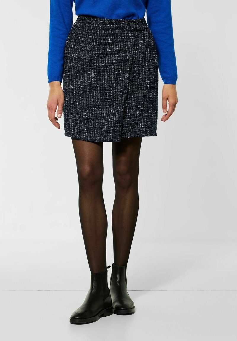 Marinblå texturerad minikjol med sidofodrad design och två knappar, tillsammans med svarta ankelstövlar och svarta genomskinliga strumpbyxor.