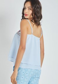 Top sin mangas de color azul claro con un diseño fluido y escote bordado. La tela parece suave, cuenta con tirantes ajustables y dobladillo en capas.