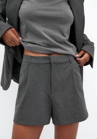 Shorts gris sur mesure en tissu texturé, avec une taille ajustée et de subtils plis à l'avant, assortis à un haut gris assorti.