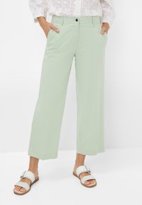 Lichtgroene wijde broek van zacht materiaal, met zijzakken en een voorknoopsluiting. G gedragen met witte instappers.