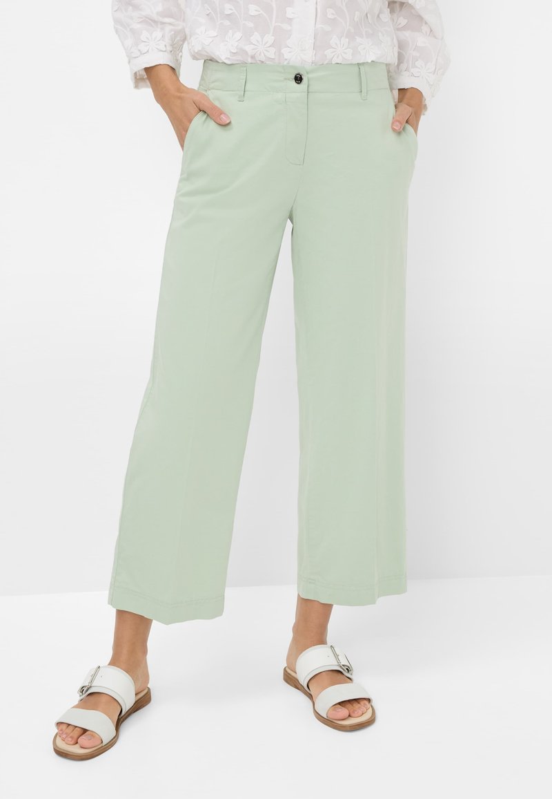 Lichtgroene wijde broek van zacht materiaal, met zijzakken en een voorknoopsluiting. G gedragen met witte instappers.