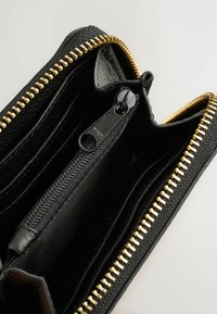 Interno di un portafoglio in pelle nera con cerniera dorata e rivestimento in tessuto, dotato di diversi scomparti per carte e di un comparto con cerniera per monete.