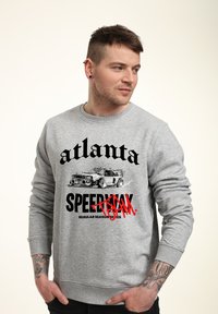 Šedá mikina s nápisem "Atlanta" a "SPEEDWAY" tučným písmem, se grafikou auta. Obsahuje žebrované manžety a lem.