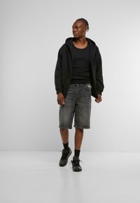 Sudadera negra con cremallera, camiseta de tirantes negra, pantalones cortos de mezclilla gris y zapatillas negras. El conjunto tiene un ajuste casual con un diseño sencillo.