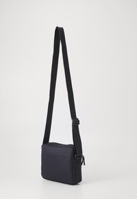 Borsa a tracolla rettangolare nera con esterno in tessuto, tracolla regolabile, chiusura con zip e design minimalista.