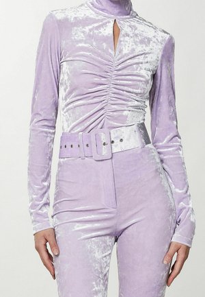 Lawendowy kombinezon z miażdżonego aksamitu z marszczonym przodem, wysokim kołnierzem, długimi rękawami oraz szerokim dopasowanym paskiem z prostokątną sprzączką.