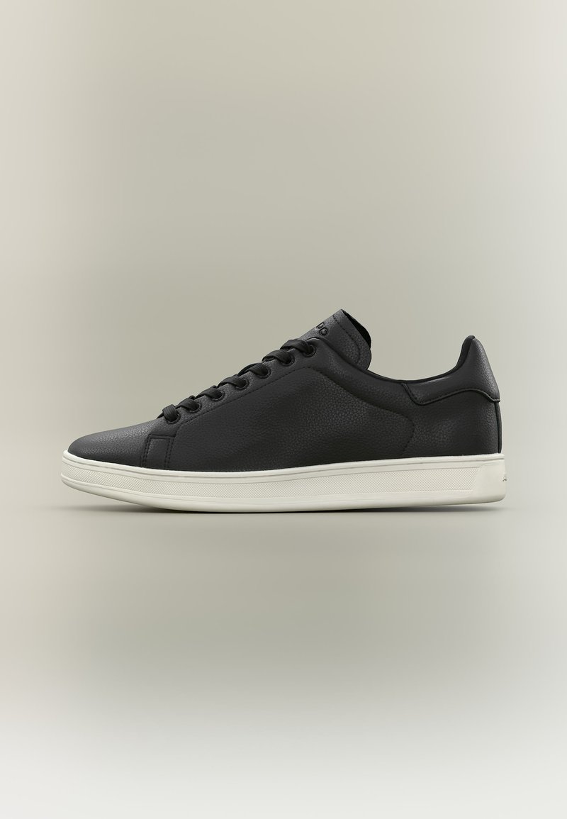 Zapatilla baja de cuero negra con cordones negros y suela de goma blanca, vista de lado sobre un fondo neutro.