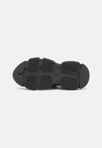Suela de zapato deportivo negro con goma texturizada, que presenta un patrón de espiga para tracción y una puntera redondeada para estabilidad.