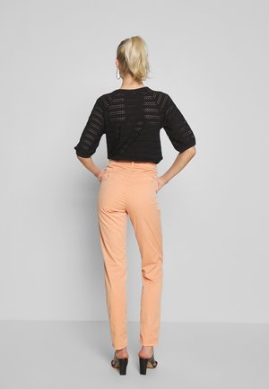 Top de punto negro con diseño calado y mangas tres cuartos, combinado con pantalones de cintura alta color durazno claro y sandalias negras de tacón.
