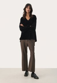 Black velvet long-sleeve top with a V-neck, paired with brown patterned trousers. Footwear features chunky black loafers. Simple, elegant look.