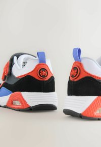 Sorte, hvide og orange sportsko med blå accenter, der har en struktureret overdel, polstret krave og et edderkop-logo på hælen.